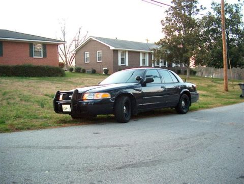 2001 Ford Crown Victoria - This black 2001 Ford Crown Victoria, equipped with a push bar, is parked on the side of a residential street.