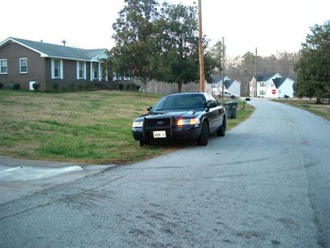 2001 Ford Crown Victoria - A black 2001 Ford Crown Victoria police car is parked on the side of a street in a residential area.