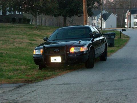 2001 Ford Crown Victoria - A black 2001 Ford Crown Victoria, equipped with a push bar, is parked on the side of a road in a suburban neighborhood.