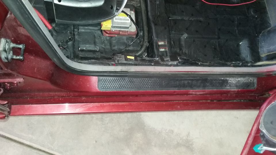 Red car door sill plate reading Pontiac with exposed body panel above