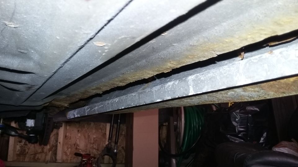 Underside of a car showing rust and damage to the frame rails