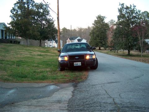 2001 Ford Crown Victoria - A black 2001 Ford Crown Victoria police car is parked on the side of a road in a suburban neighborhood.