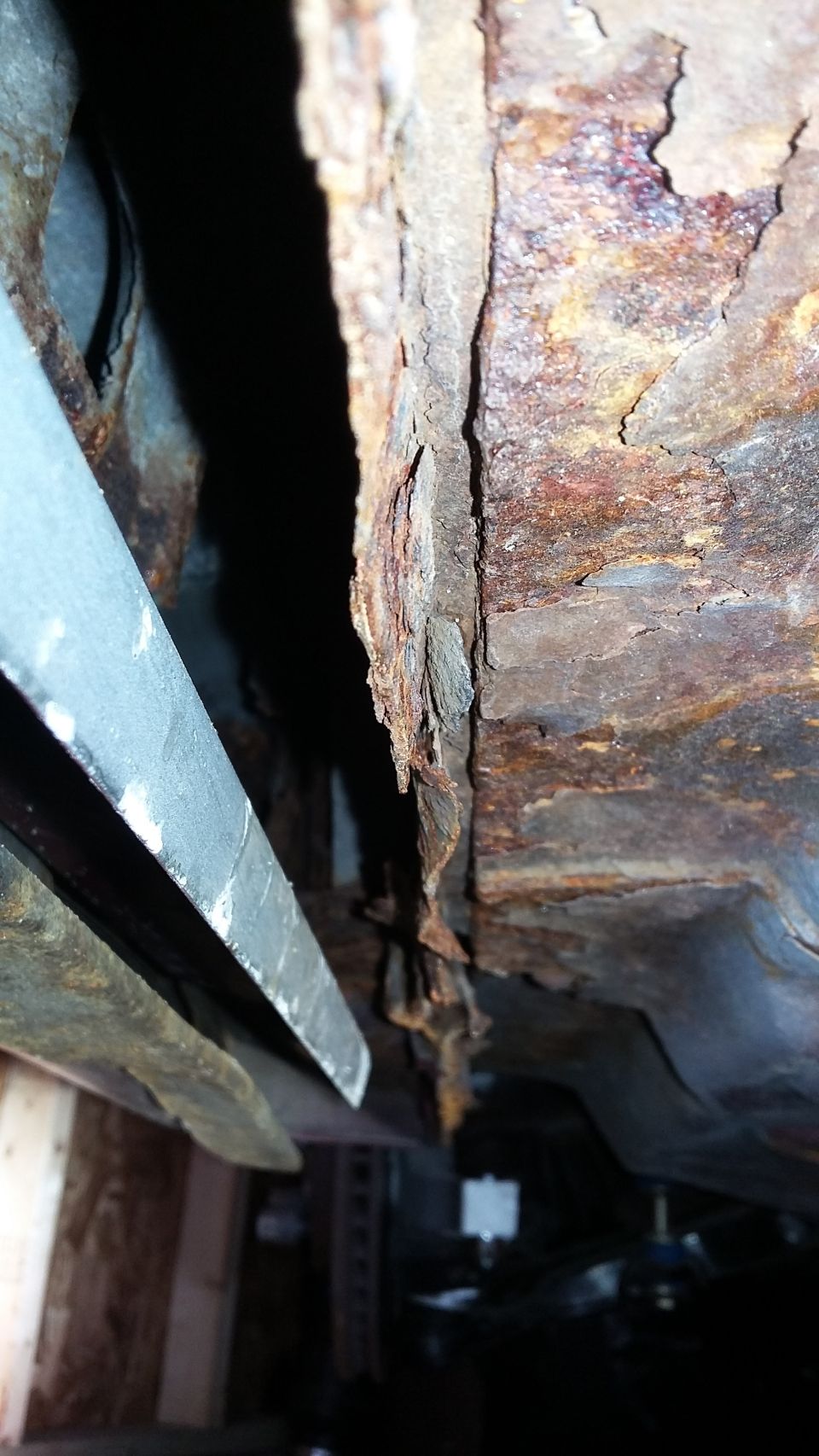 Heavily rusted car frame section with visible metal fatigue and decay