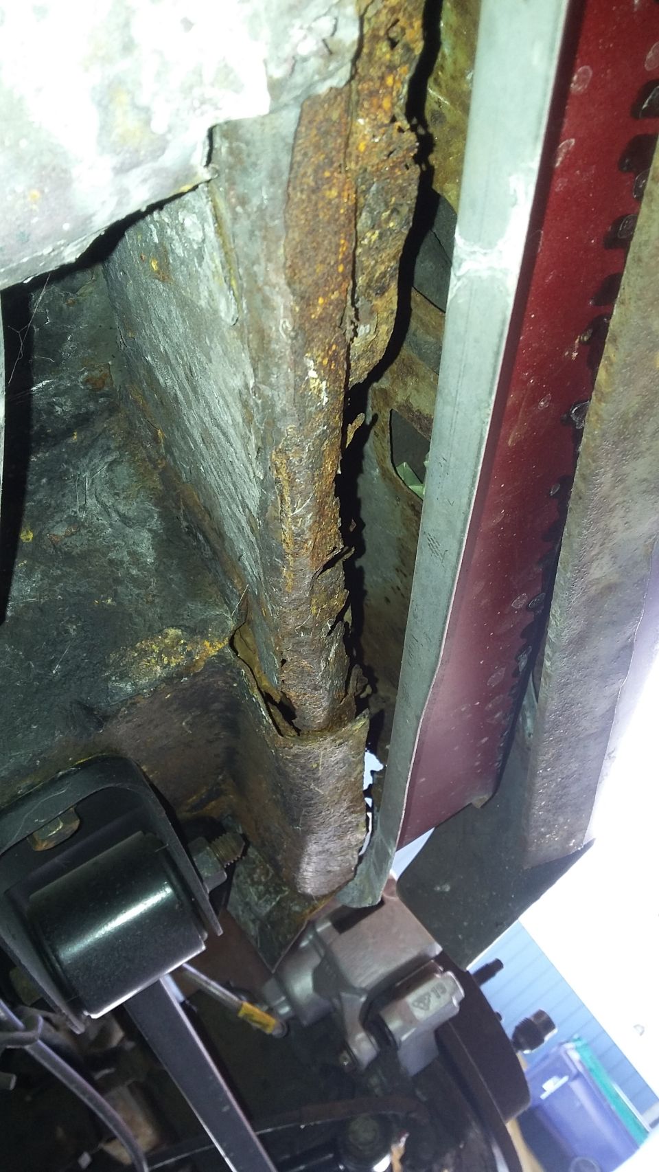 Rusted frame rail and brake caliper on a red vehicle underside