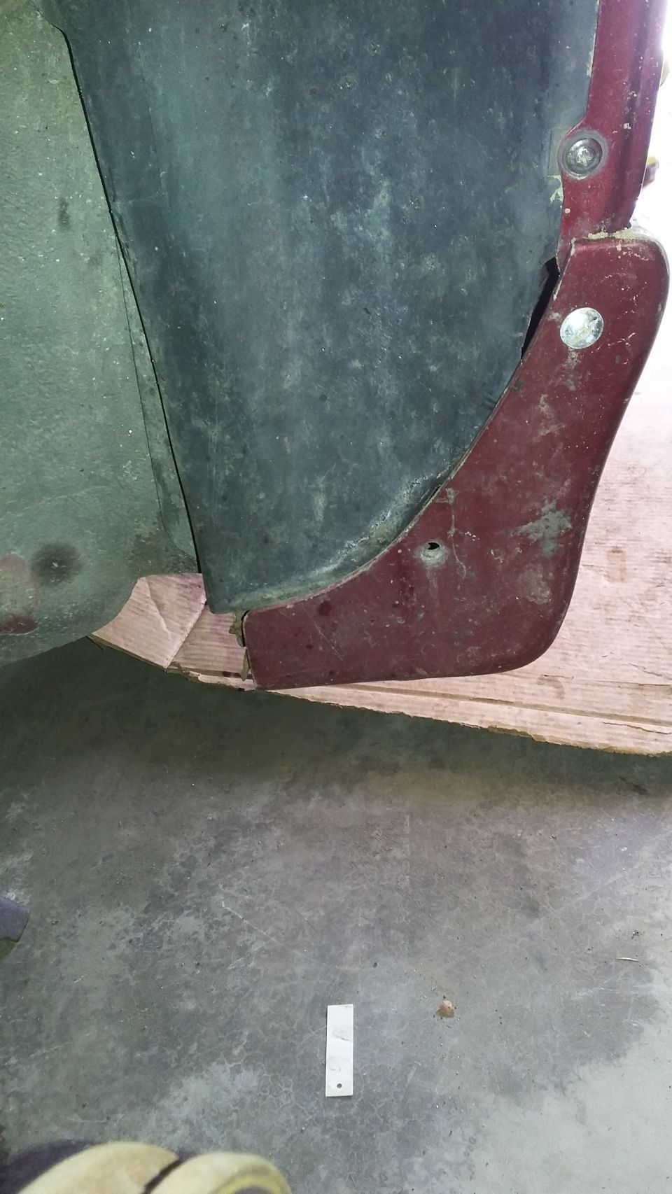 Close-up of a dark car fender liner and a maroon trim piece attached with screws