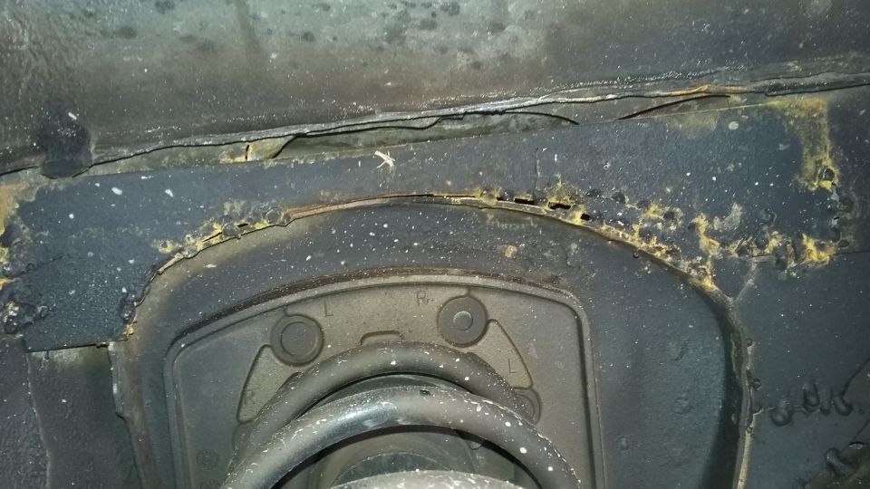 Close-up of heavily rusted metal frame and suspension component on a vehicle. Shows significant corrosion and wear