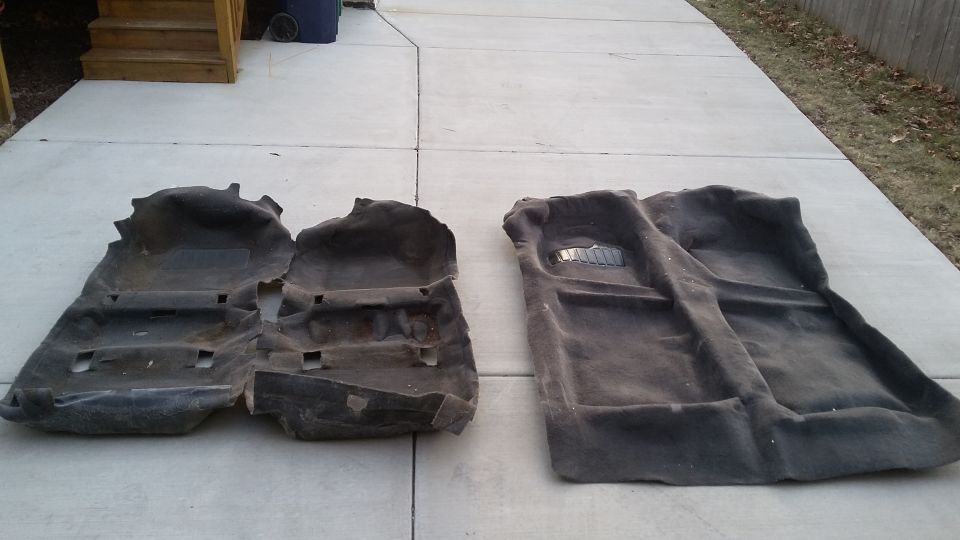 Two dark gray car floor mats laid out on a concrete driveway