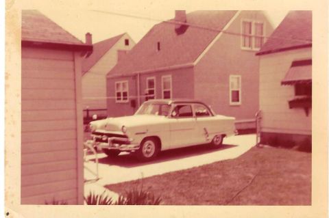 1996 Ford Bronco - A vintage sedan is parked in a residential driveway, with houses on either side.
