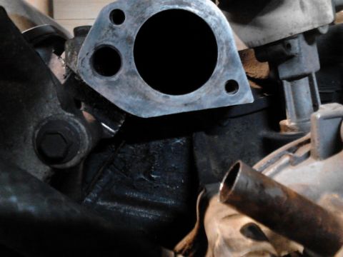 1995 Ford Bronco - Close-up view of an engine's exhaust manifold flange, showing its mounting holes and a connected pipe.