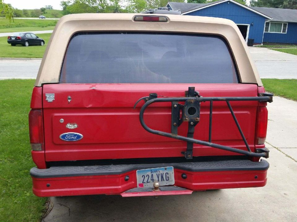 Rear view of a red 1996 Ford Bronco with a tan top and a spare tire carrier mounted on the back