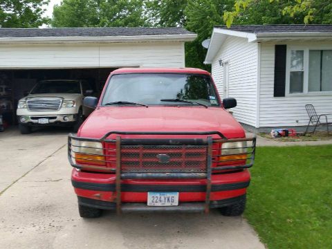 1996 Ford Bronco - This red 1996 Ford Bronco is parked in front of a garage, with another vehicle visible inside.