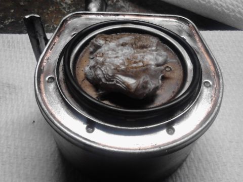 1995 Ford Bronco - A close-up view of a dirty automotive part, possibly a filter housing or cap.
