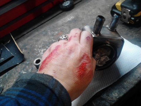 1995 Ford Bronco - A hand with cuts and blood holds a metal car part with two hose fittings, resting on a paper towel.