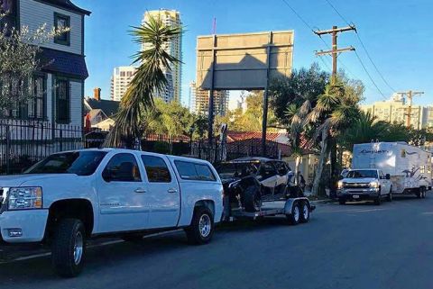 1988 Ford Bronco - Multiple vehicles are seen on a street, including a white pickup truck towing a trailer with a side-by-side and another pickup truck towing…