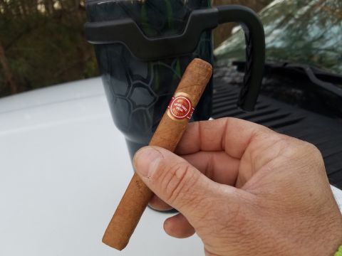 2018 Ford Bronco - A hand holds a cigar next to a travel mug, with a vehicle's windshield visible.
