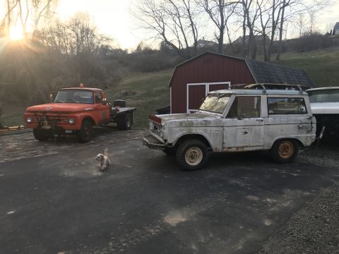 1967 Ford Bronco - A white Ford Bronco and an orange Ford F-series truck sit in a driveway next to a red barn.