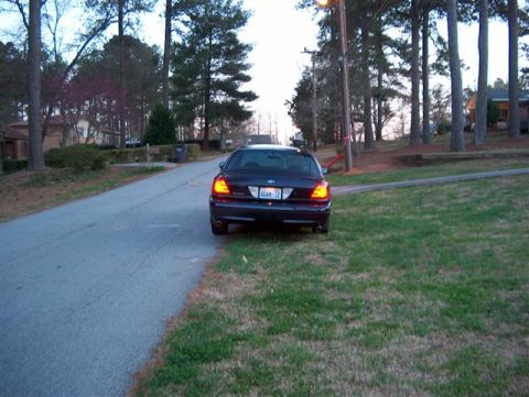 2001 Ford Crown Victoria - Rear view of a dark 2001 Ford Crown Victoria parked on the grass next to a residential street.