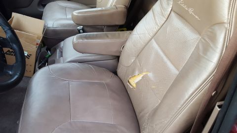 1967 Ford Bronco - The interior of a vehicle shows a torn leather driver's seat with "Eddie Bauer" embroidery.