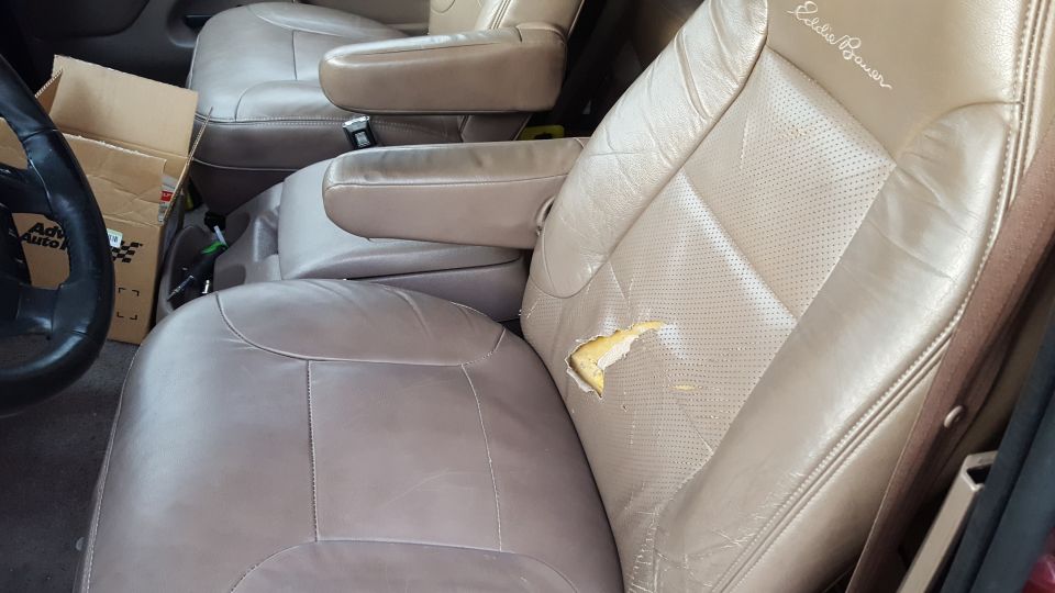Torn leather driver's seat in a vehicle interior with "Eddie Bauer" stitched on it