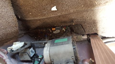 1967 Ford Bronco - A close-up view of the messy under-seat area of a vehicle, showing wiring and a discarded battery.