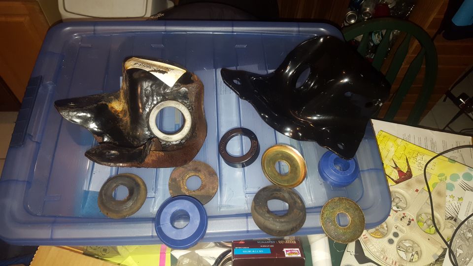 Two black automotive parts and several metal and plastic washers on a blue plastic bin