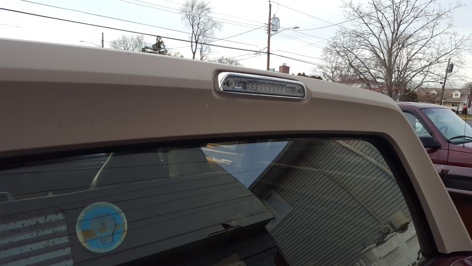 Tan SUV rear window and roofline with chrome-trimmed LED third brake light