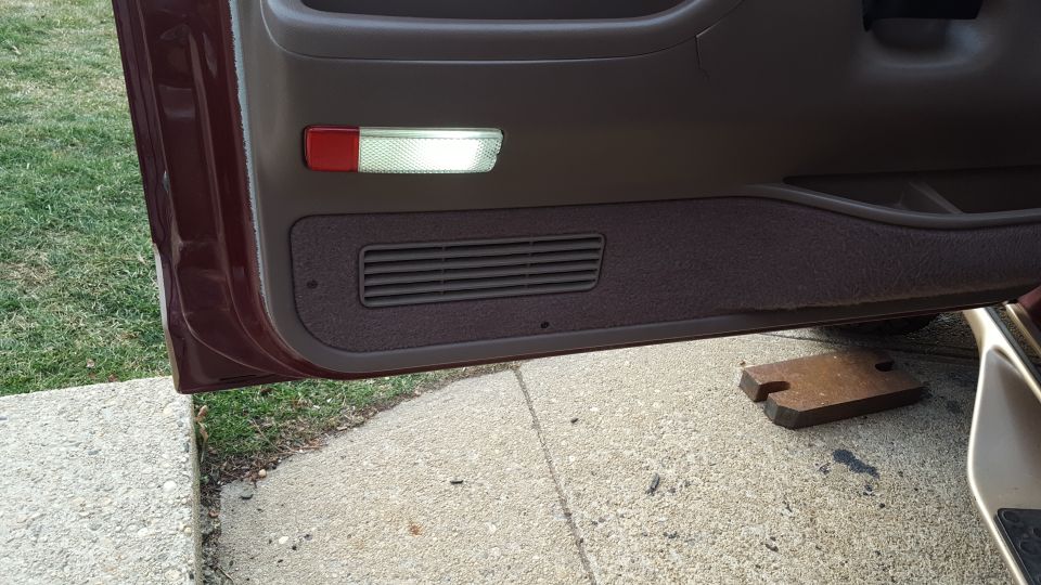 Maroon car door interior with a rectangular speaker grille and a red and white interior light
