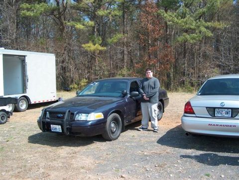 2001 Ford Crown Victoria - A man poses with his Ford Crown Victoria at an outdoor event, with another vehicle and a trailer nearby.