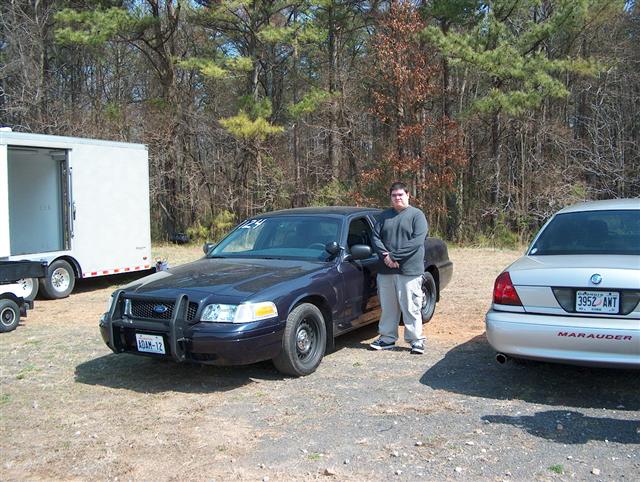 Dark blue Crown Victoria with push bar on gravel, man standing at driver's door