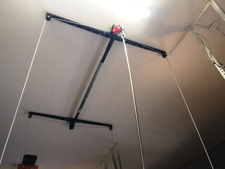 Garage door opener mechanism with cables and a red component, mounted on a white ceiling