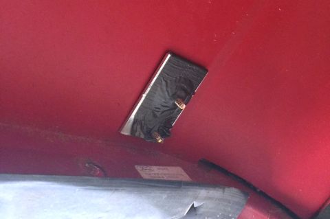 1994 Ford Bronco - A metal bracket is affixed with black tape and screws to a red painted surface, possibly part of a vehicle's interior or exterior.