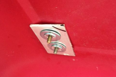 1994 Ford Bronco - Close-up of a metal plate with bolts and washers on a red background.