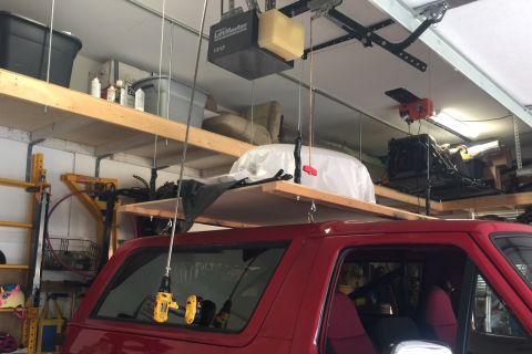1994 Ford Bronco - A red SUV is parked in a garage with tools suspended above it.