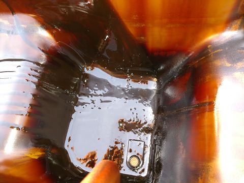 1996 Ford Bronco - Close-up view of an oil pan, showing dark, used oil and the drain plug.