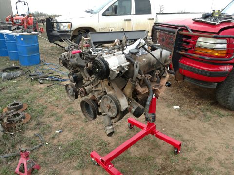 1996 Ford Bronco - Engine removed from a vehicle and placed on a red stand, with other vehicles visible in the background.