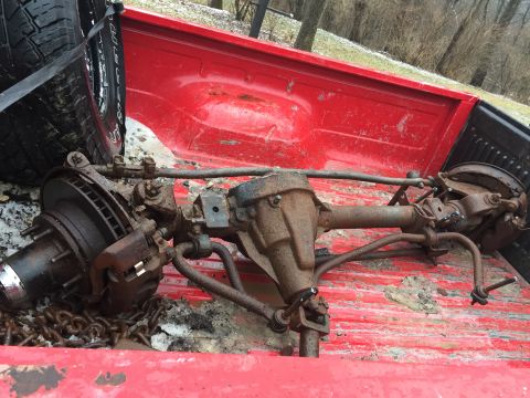 1967 Ford Custom Wagon - Front axle assembly with disc brakes and suspension components loaded in a red pickup truck bed.