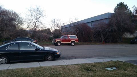 1985 Ford Bronco - A red and tan 1985 Ford Bronco is parked on the side of the road next to a black sedan.