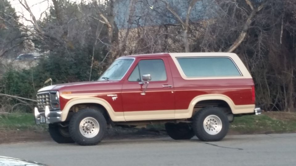 Red and tan 1985 Ford Bronco parked on the side of the road