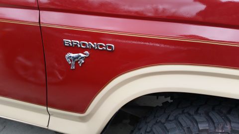 1985 Ford Bronco - Close-up side view of a red Ford Bronco with chrome badging that reads "BRONCO" and a chrome horse emblem. The vehicle features a two-tone…