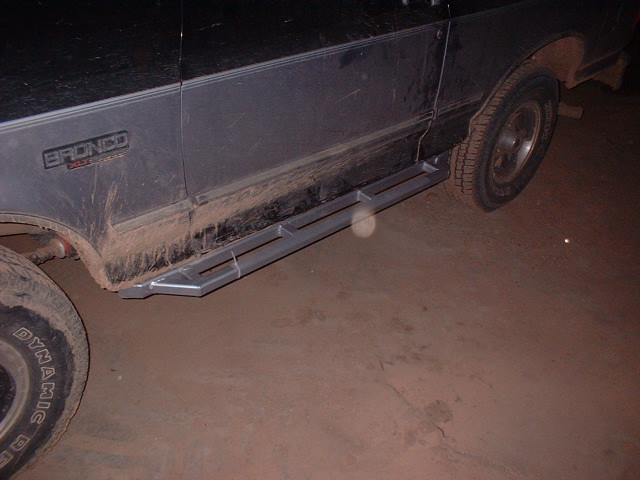 Mud-caked Bronco rocker panel and tubular step bar at night with dirt floor