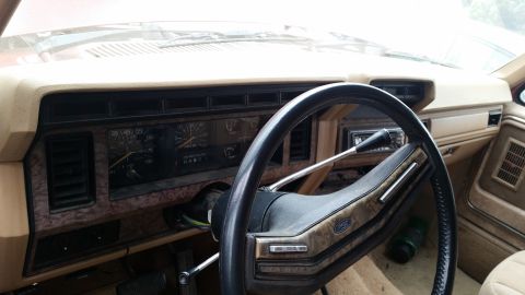 1985 Ford Bronco - The interior of a vintage Ford truck or SUV, featuring a tan dashboard, a wood-grain trim steering wheel with a Ford logo, and a cluster of…