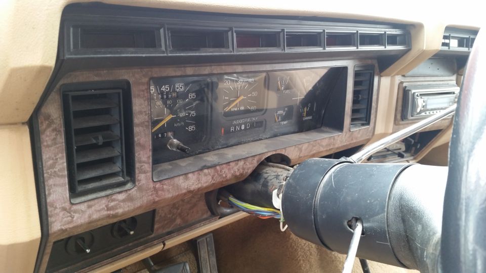 Interior of a vintage Ford truck or SUV dashboard with gauges, air vents, and exposed steering column wiring.