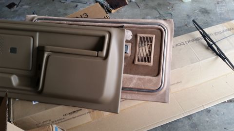 1985 Ford Bronco - A tan-colored interior door panel is laid out on top of a cardboard box. Another section of the vehicle's interior, featuring a vent and sp…