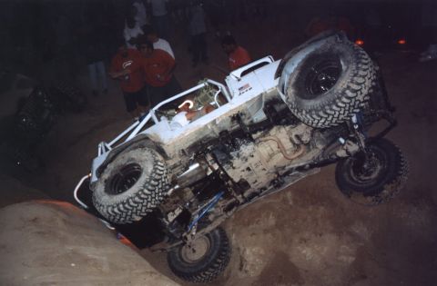 2000 Ford F-450 - White Jeep buggy up on its side against a rock at a night crawling event, exposing the undercarriage, driveshaft, exhaust, skid plate, blue…
