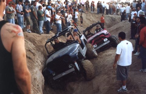 2000 Ford F-450 - Two open-top Jeeps, a gray CJ/Wrangler with a black roll cage in front and a pink one behind, pick their way down a steep dirt gully while…