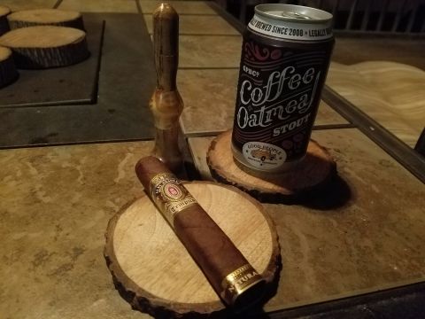 2018 Ford Bronco - A cigar rests on a wooden coaster next to a can of Coffee Oatmeal Stout. A wooden tool is also visible.