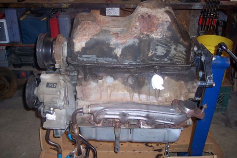 1995 Ford Bronco - A disassembled engine, likely from a 1995 Ford Bronco, is mounted on a blue engine stand in a workshop. The engine block and oil pan are vi…