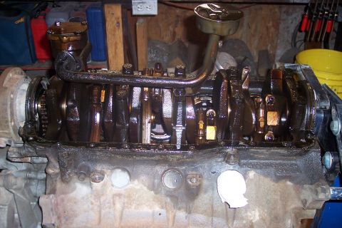 1995 Ford Bronco - A heavily oiled internal engine component, likely a crankshaft and oil pickup tube, is shown in a workshop setting. The engine block is par…
