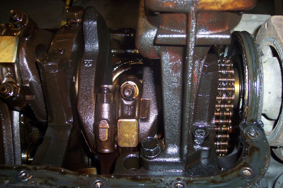 Close-up of oily engine crankshaft, connecting rods, and timing chain.
