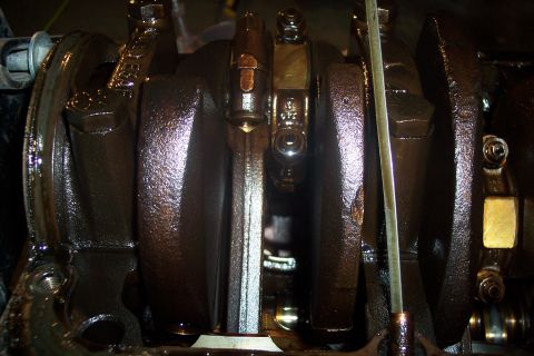 1995 Ford Bronco - A close-up view of the crankshaft and connecting rods of an engine, coated in dark oil. The metal components show signs of wear and use.